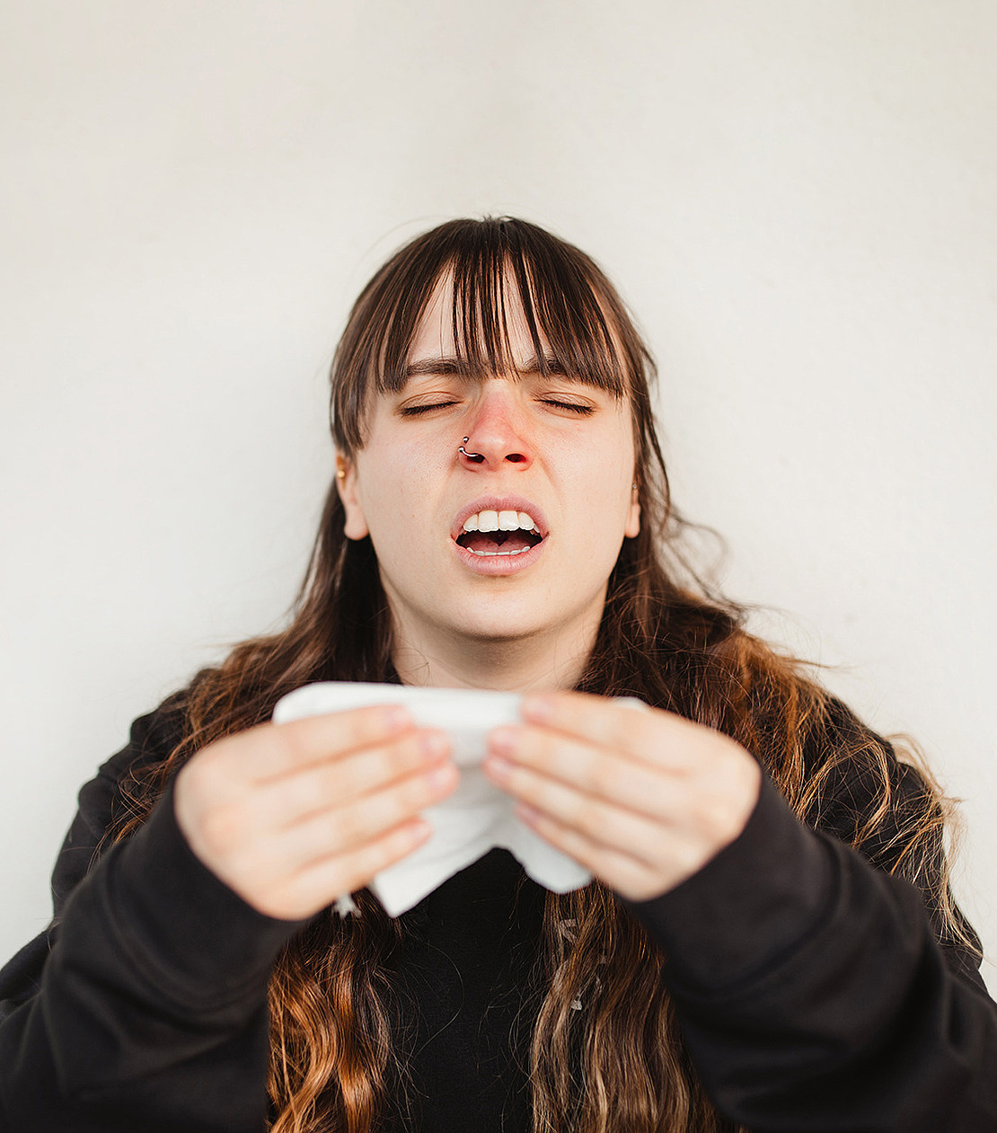 Eine Frau ist krank und niest. Im Text geht es darum, an welche Anlaufstelle man sich im Krankheitsfall wenden kann.