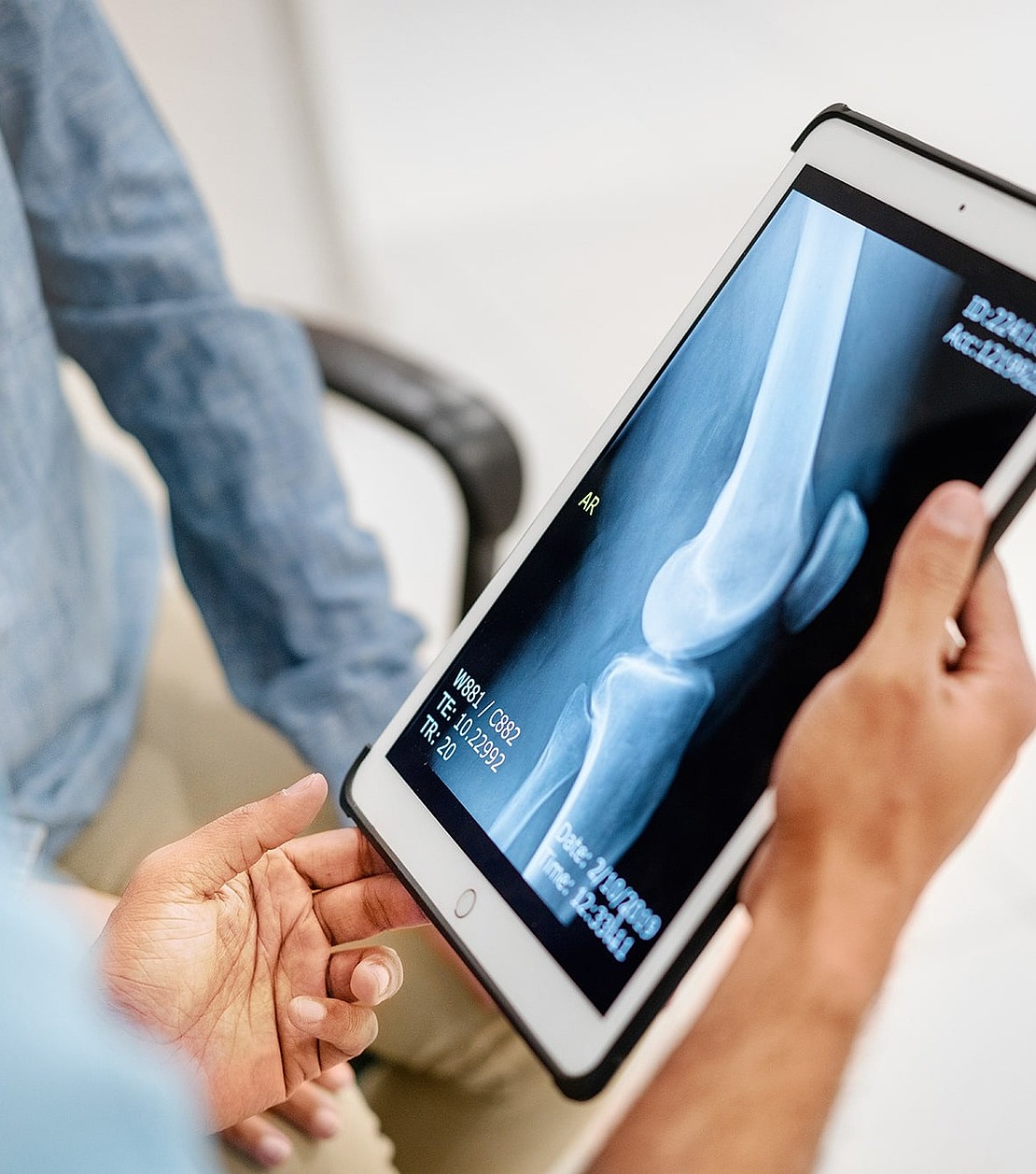 Eine Person hält ein Tablet in der Hand, auf dem ein Röntgenbild eines Knochens zu sehen ist, während eine andere Person in der Nähe sitzt und eine medizinische Beratung oder eine Diskussion über die Röntgenergebnisse vorschlägt.