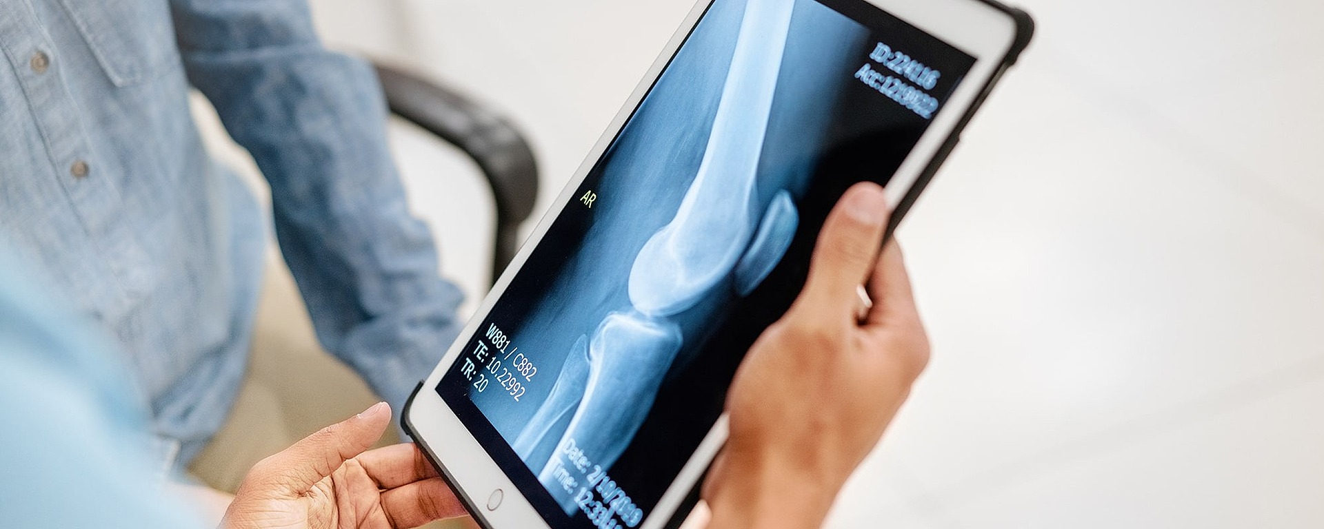 Eine Person hält ein Tablet in der Hand, auf dem ein Röntgenbild eines Knochens zu sehen ist, während eine andere Person in der Nähe sitzt und eine medizinische Beratung oder eine Diskussion über die Röntgenergebnisse vorschlägt.
