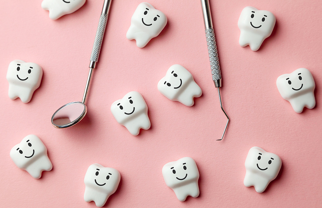 Auf einer rosafarbenen Fläche sind zahnförmige Figuren mit lächelnden Gesichtern verteilt, daneben ein Zahnspiegel und eine Zahnsonde.