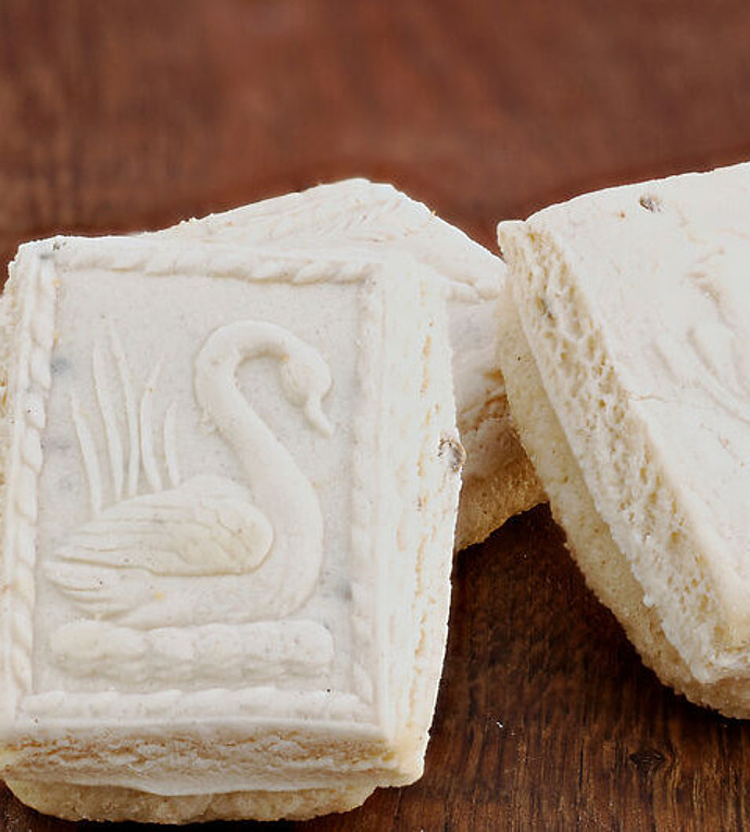 Rechteckige Kekse mit einem detaillierten Schwanenmotiv sind auf einer Holzoberfläche gestapelt. Die Kekse sind blass und haben eine leicht krümelige Textur.