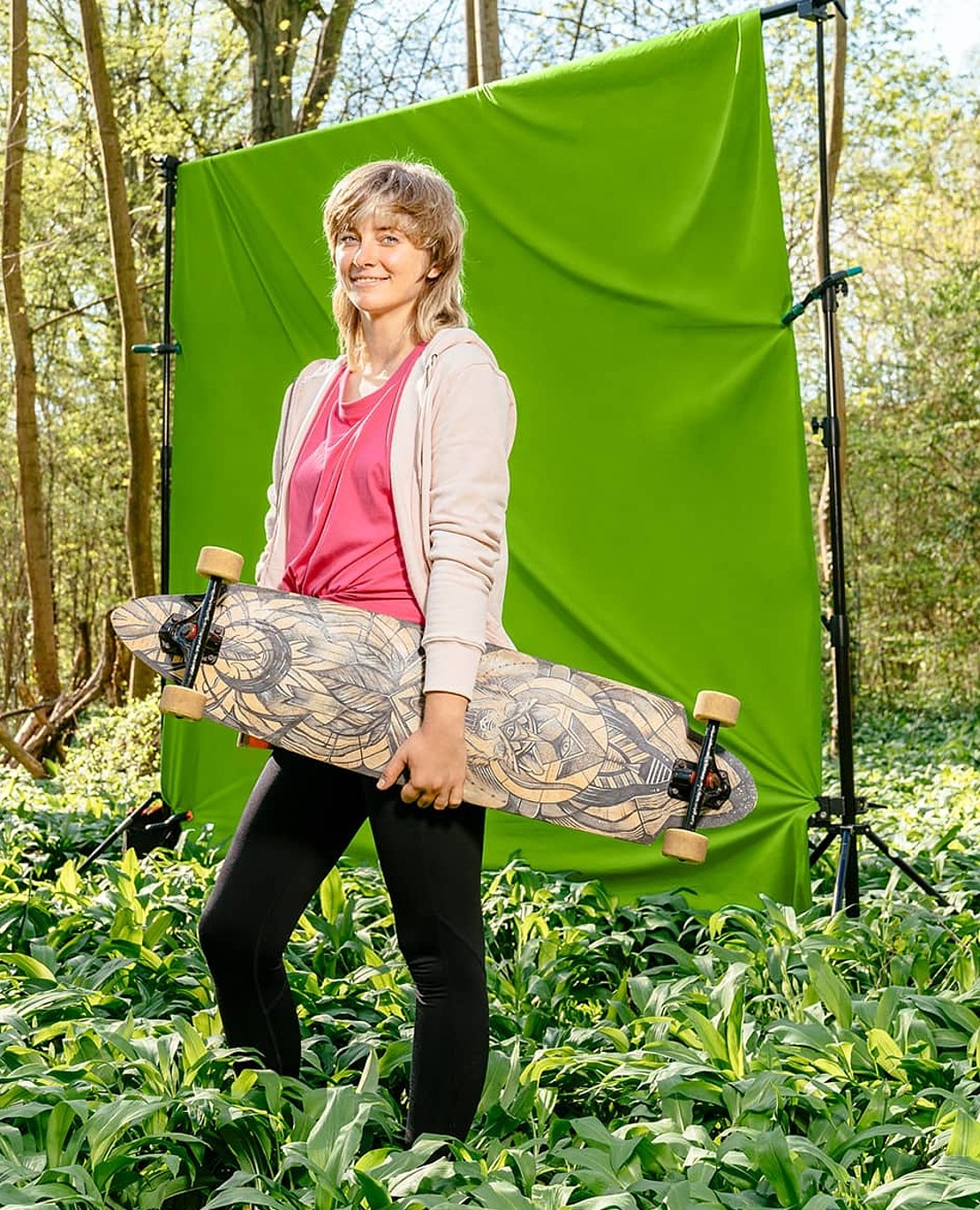 Frau mit Longboard in der Hand vor grünem Hintergrund