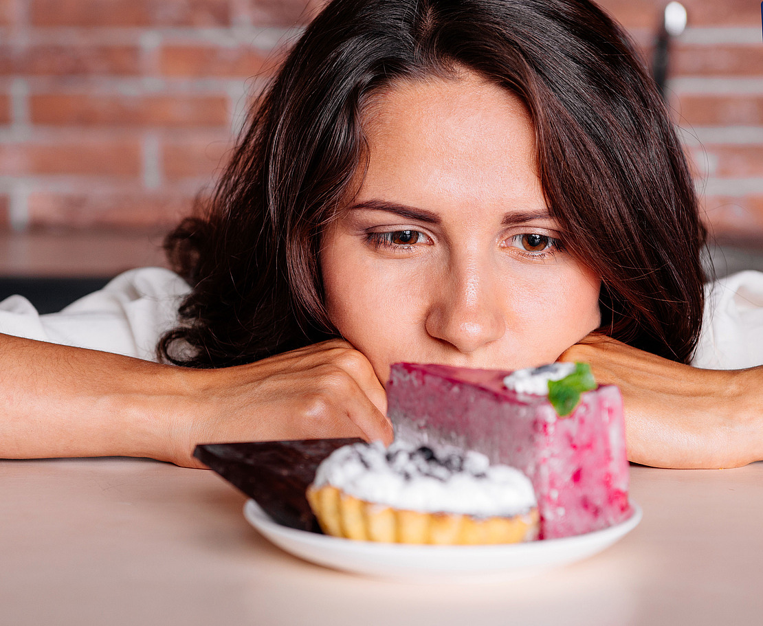Frau starrt auf einen Teller mit süßen Leckereien