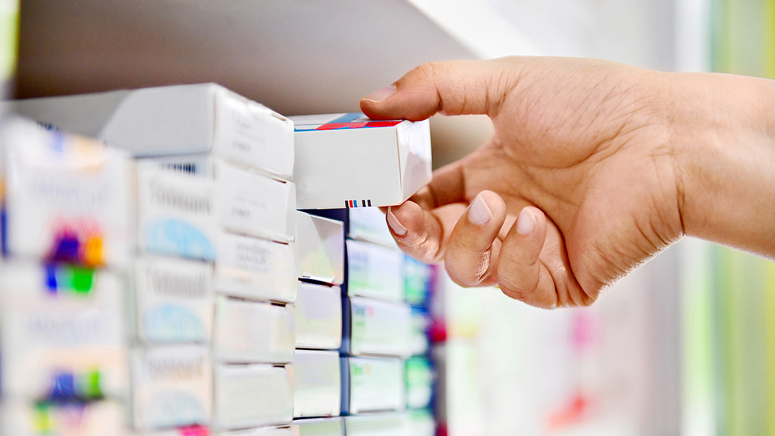 Hand nimmt eine Arzneimittelschachtel aus einem Regal