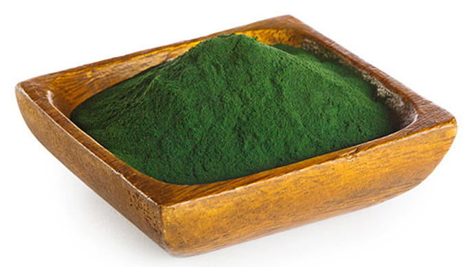 Eine kleine Holzschale, gefüllt mit einem Hügel aus feinem, dunkelgrünem Pulver, isoliert auf weißem Hintergrund.
