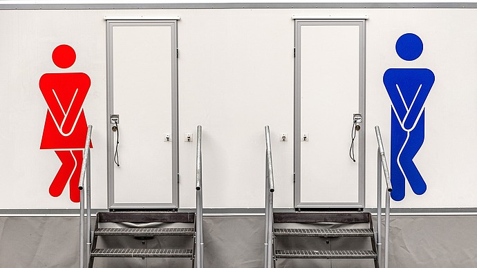Zwei Toilettentüren mit Treppen; eine hat ein rotes weibliches Symbol und die andere ein blaues männliches Symbol, beide mit gekreuzten Beinen, die die Dringlichkeit anzeigen.