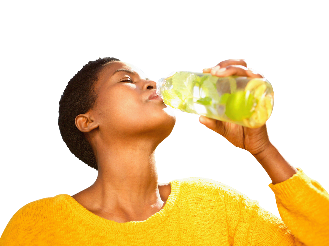 Eine Person in einem gelben Pullover trinkt vor einem weißen Hintergrund Wasser aus einer durchsichtigen Flasche mit Zitronenscheiben und Kräutern.