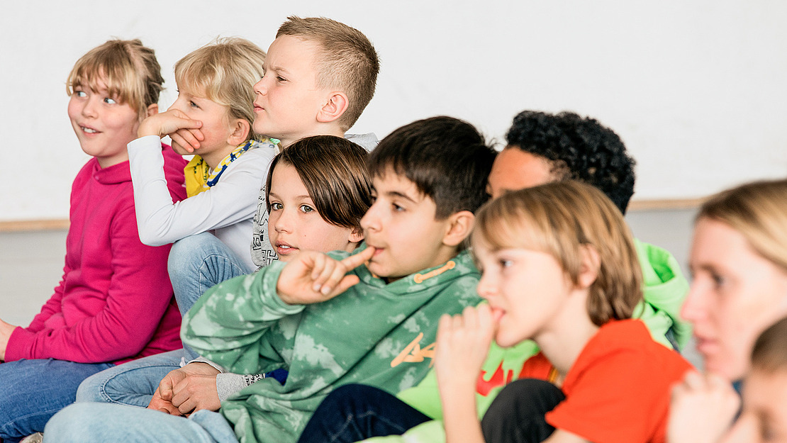 Schulkinder sitzen in einer Reihe und hören zu.