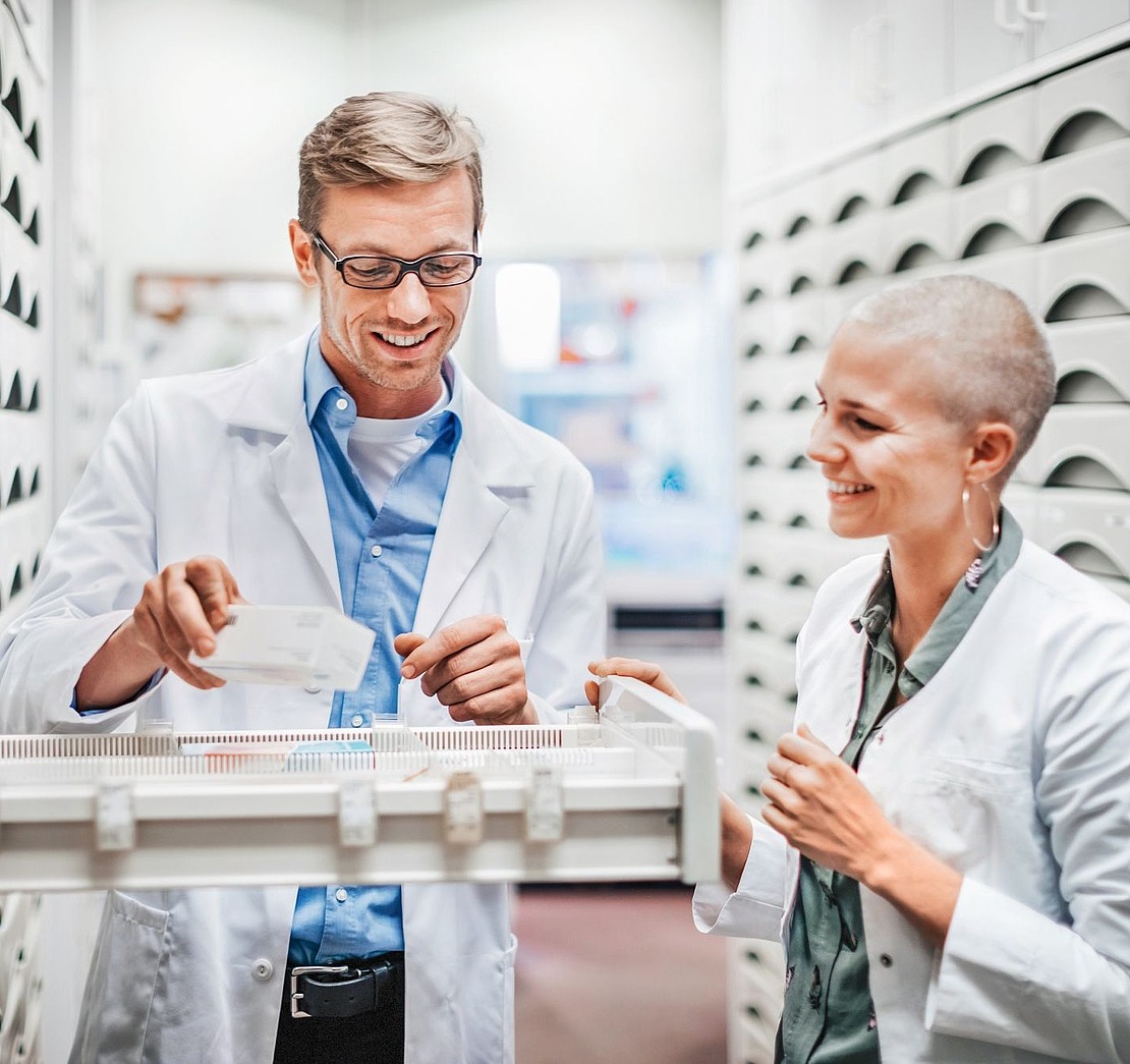 Apotheker und Apothekerin stehen an einem Schrank in der Apotheke
